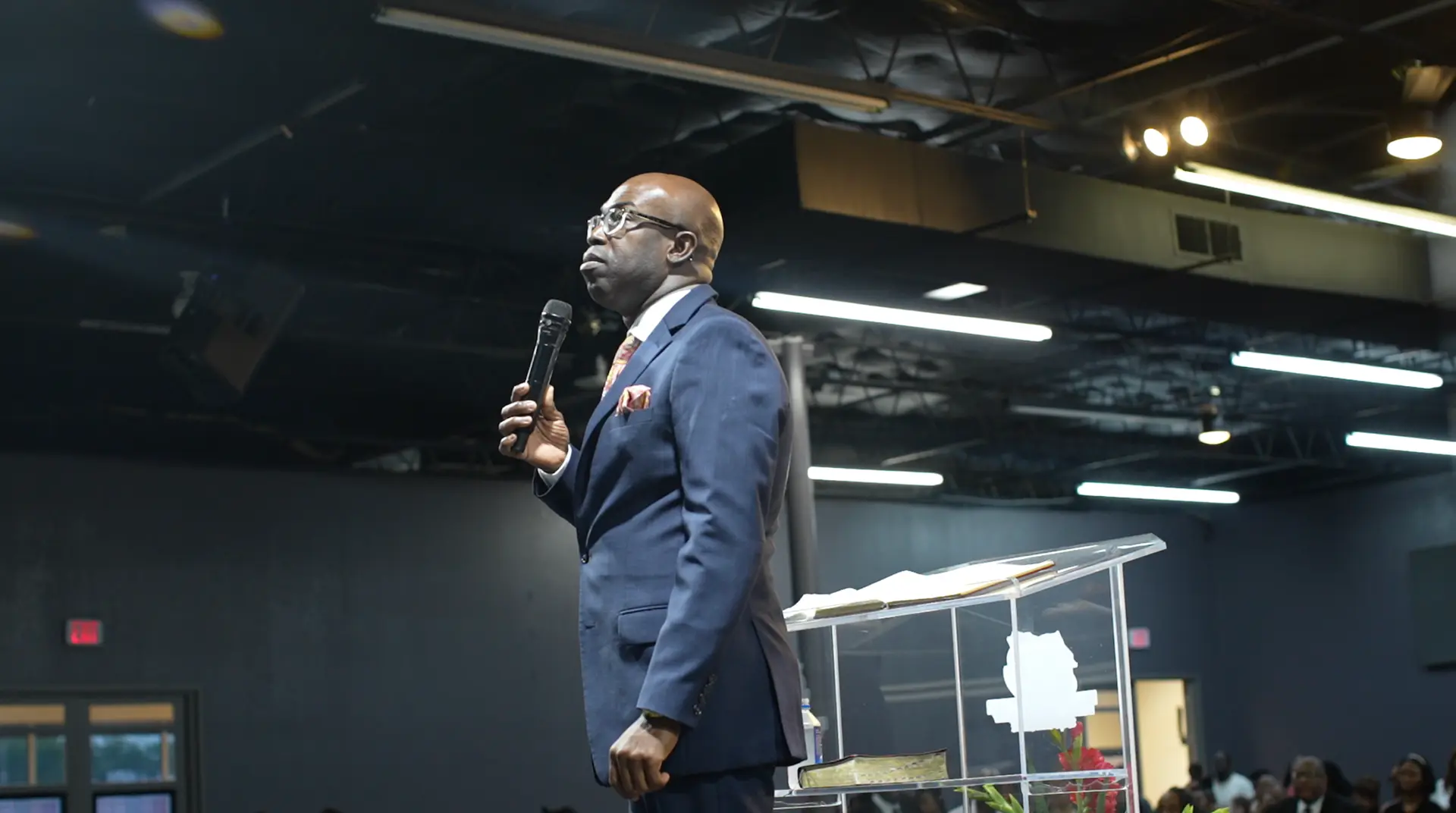 Apostle Frank Manu preaching with a microphone beside the pulpit